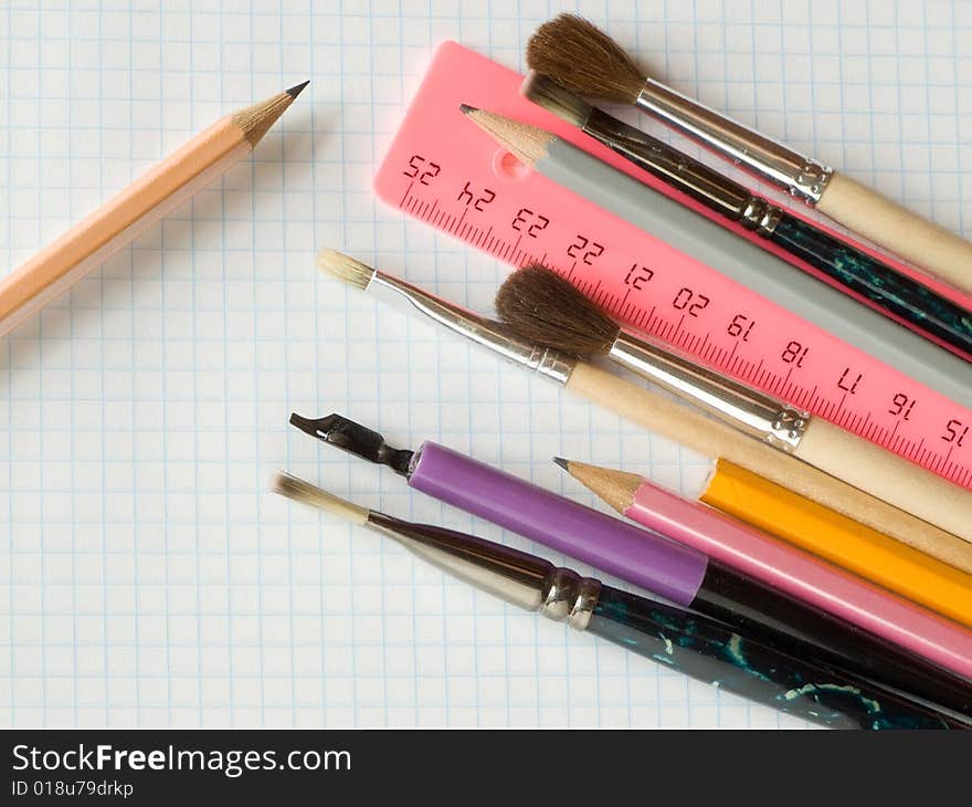 Pencils and brushes on squared sheet of a copybook. Pencils and brushes on squared sheet of a copybook