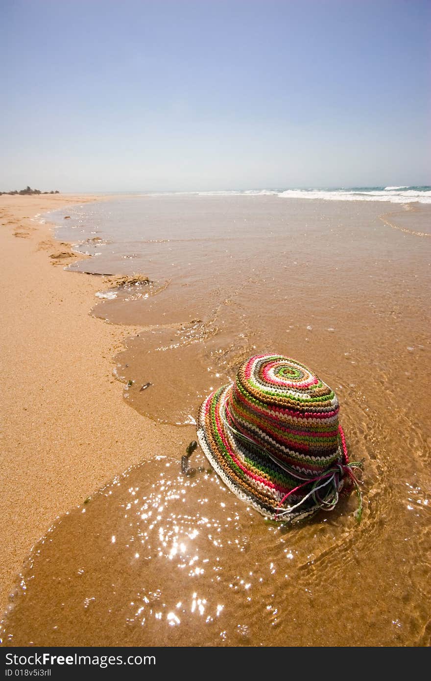 Colored sun hat on water edge on deserted beach. Colored sun hat on water edge on deserted beach