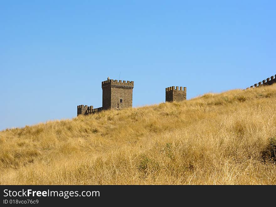 Old medieval stronghold uprising behind a yellow hill against blue sky background. Old medieval stronghold uprising behind a yellow hill against blue sky background