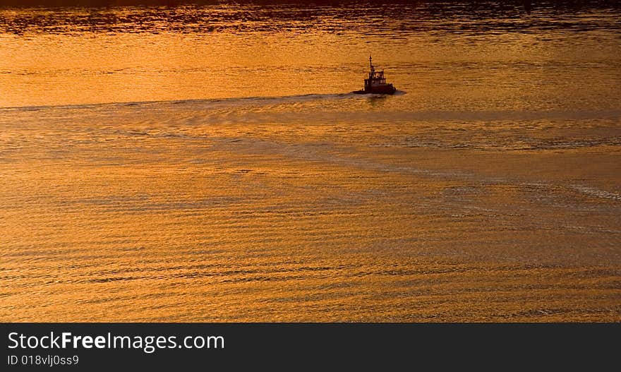 A pilot or tug boat moving through a bay in the golden light of dawn. A pilot or tug boat moving through a bay in the golden light of dawn