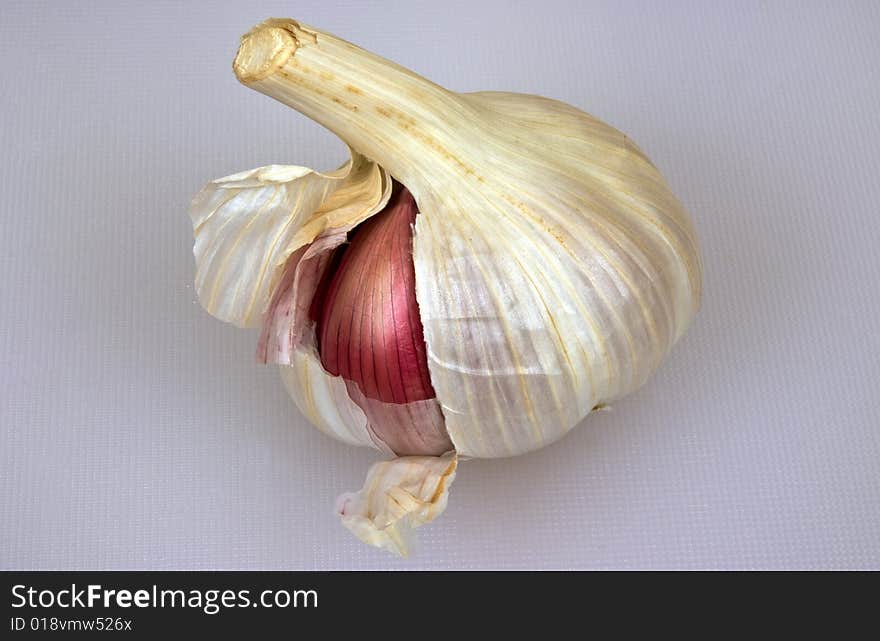 A garlic bulb with one red clove showing. A garlic bulb with one red clove showing