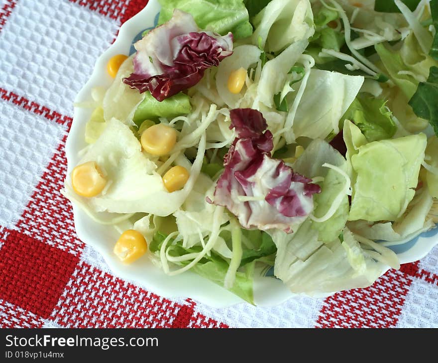 Green salad with corn in a plate on checked table cover, closeup