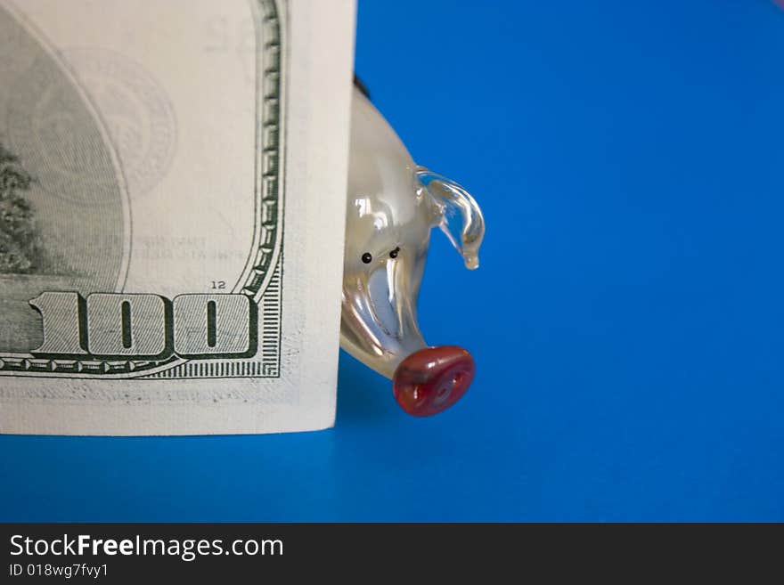 Glass piglet and hundred dollars on the blue background. Glass piglet and hundred dollars on the blue background