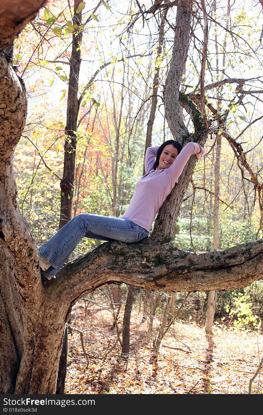 Pretty teen reclining on a large tree branch in the woods