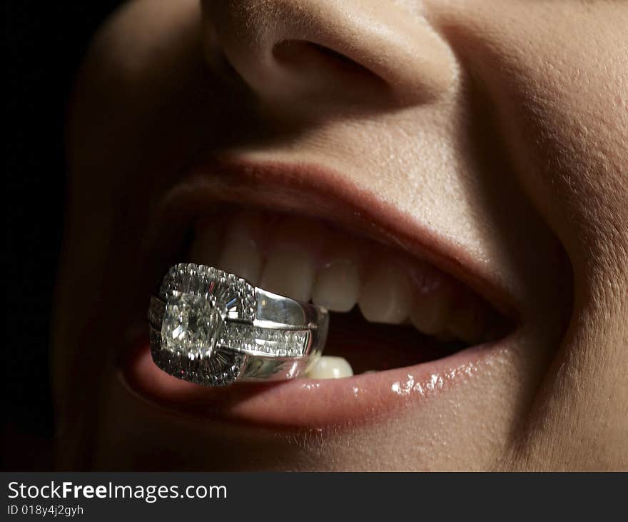 Close up shot of sensual lips holding a diamond ring. Close up shot of sensual lips holding a diamond ring