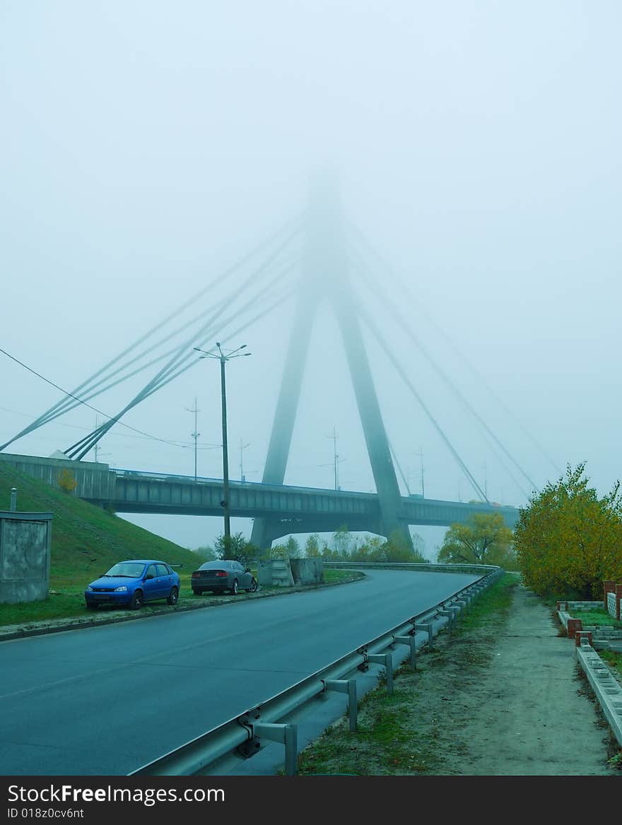 Industrial constructions are in fog, details of bridge are in a grey color