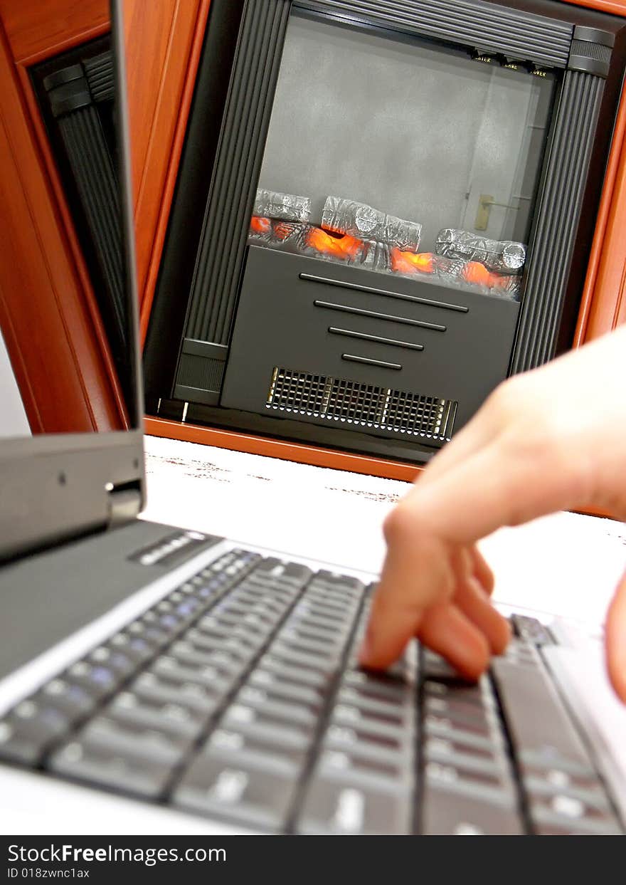 Close up of hand on the laptop keyboard and the fireplace in the background.