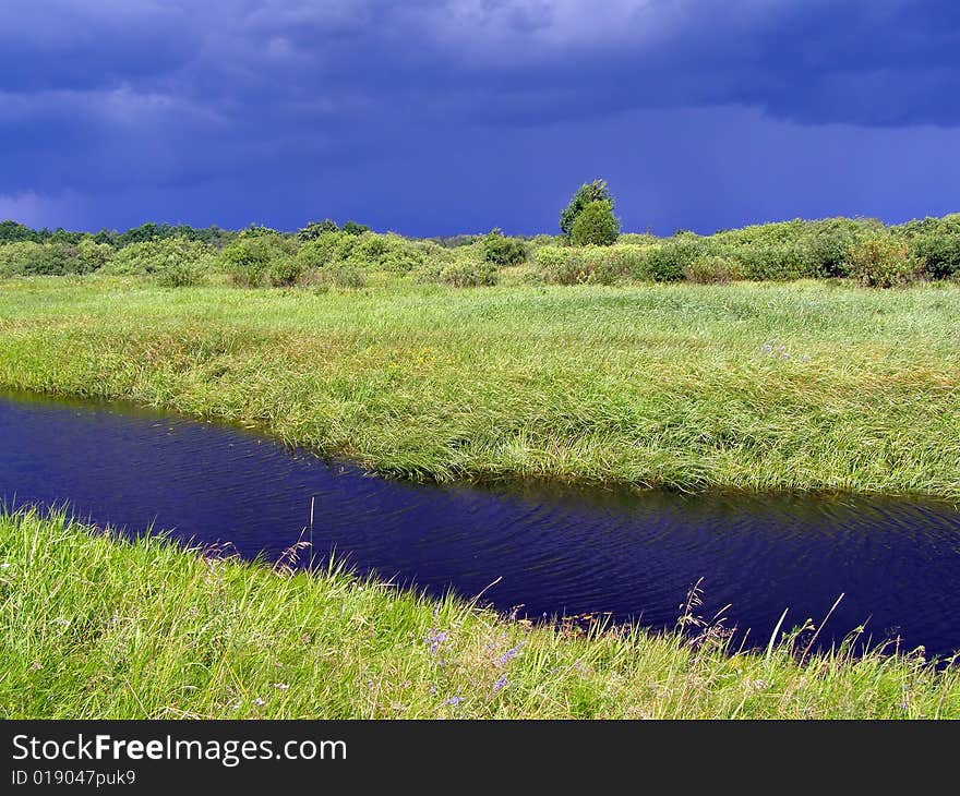 Small river on green field before thunderstorm