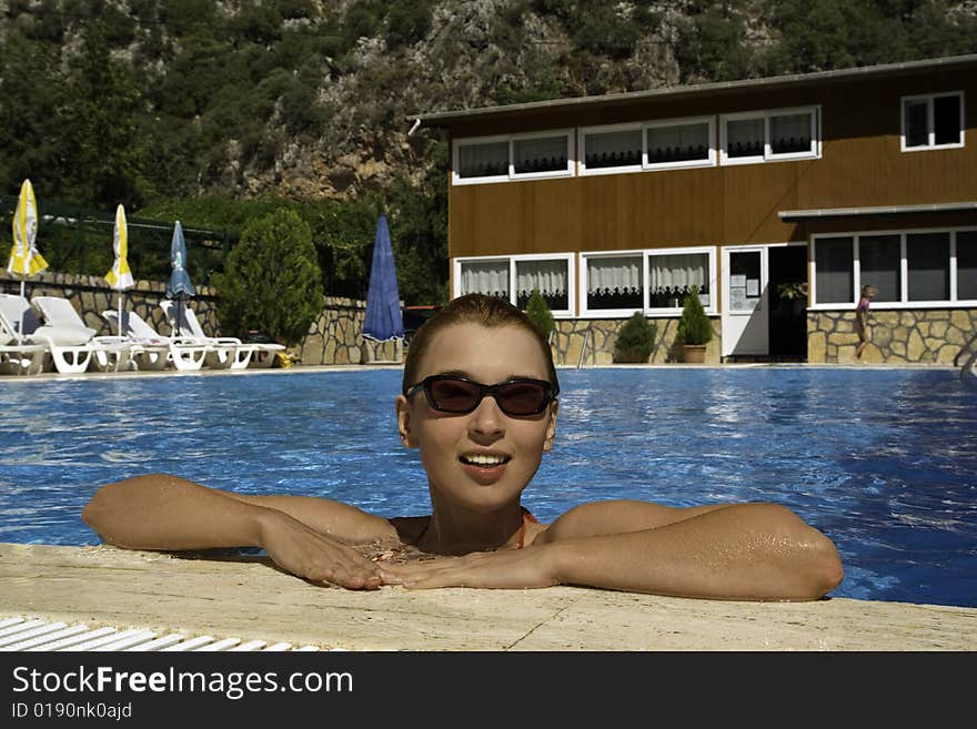 Young tanned smiling woman in sunglasses in the swimming pool. Young tanned smiling woman in sunglasses in the swimming pool