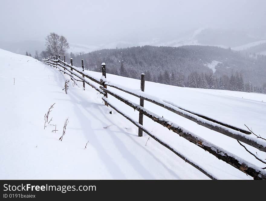 Snowy field and fence in winter mountains