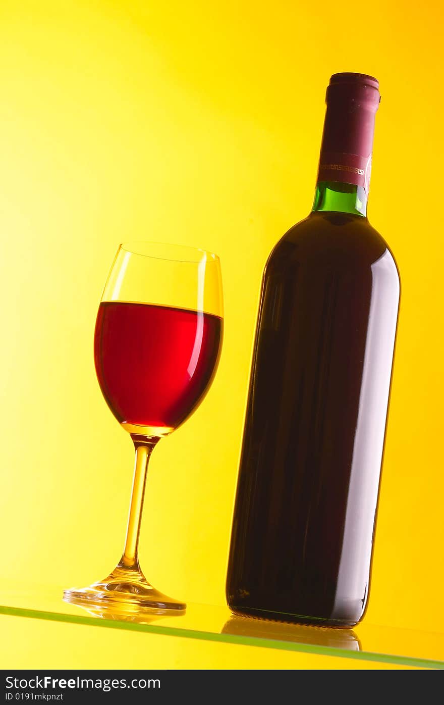 Glass and bottle of red wine on yellow background