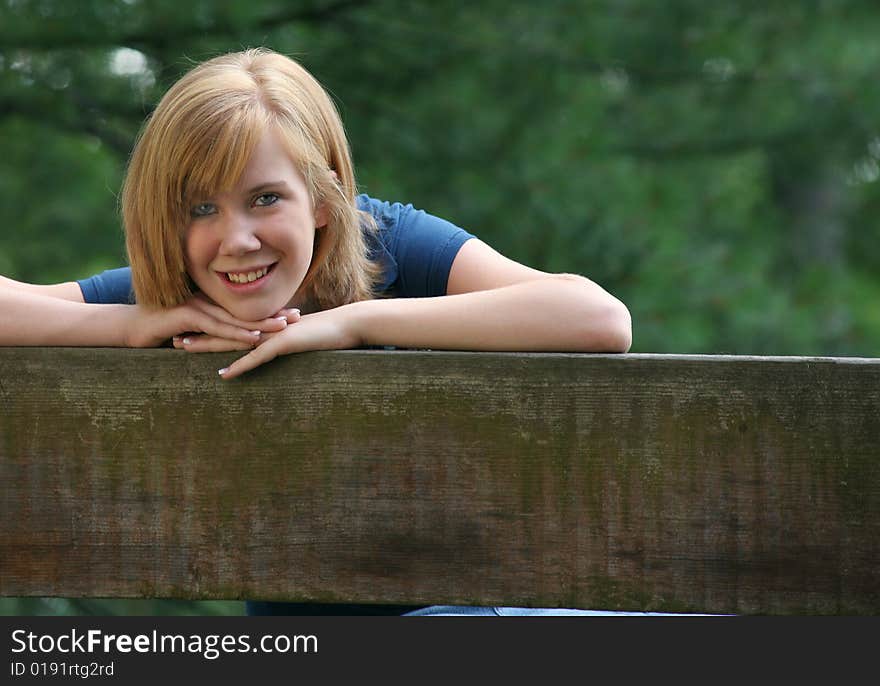 Teenage girl leaning on the back of a bench smiling with space on right and bottom for copy. Teenage girl leaning on the back of a bench smiling with space on right and bottom for copy.