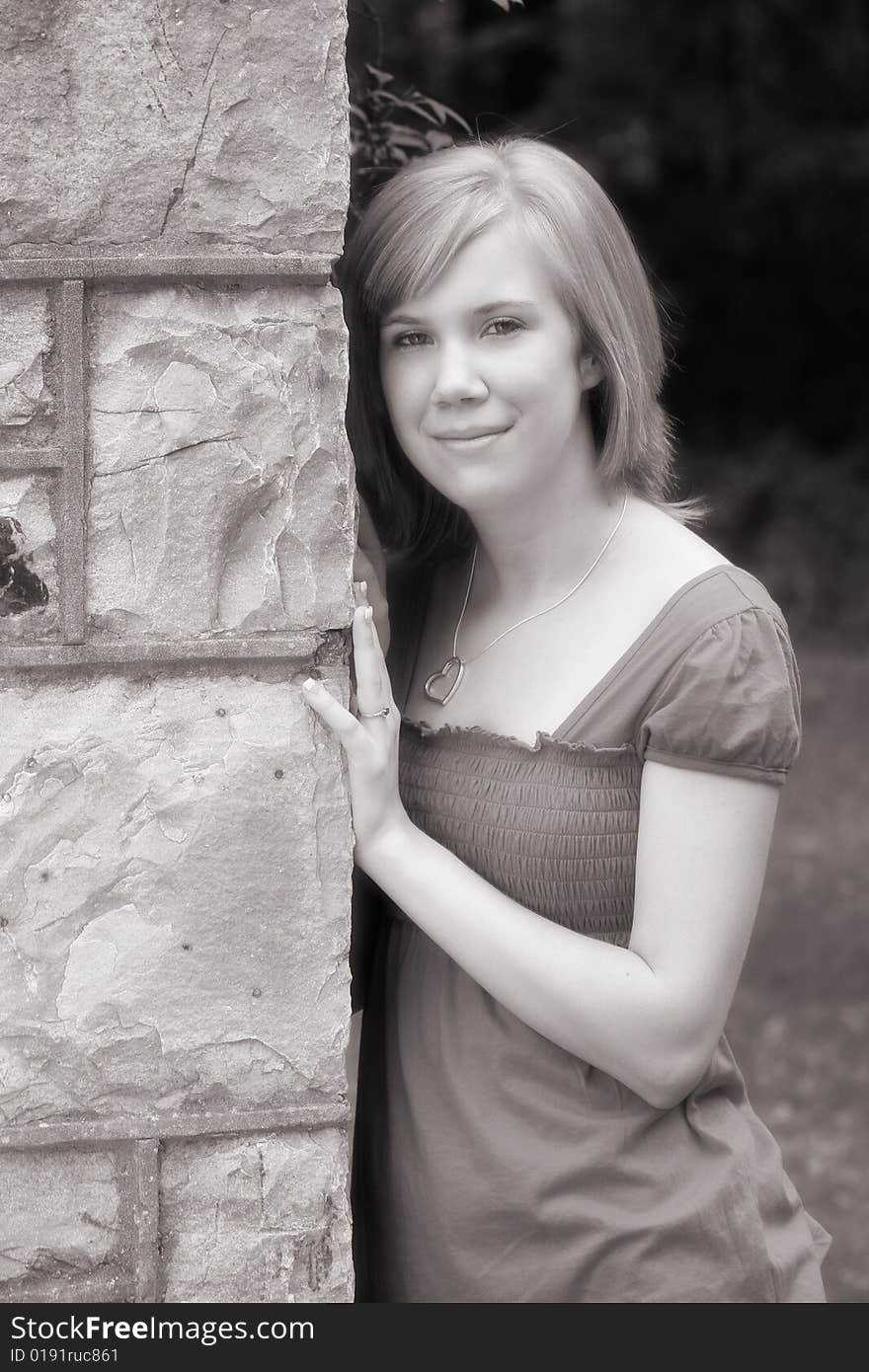 A teenage girl leans against a large outdoor fireplace in a simple black and white image. A teenage girl leans against a large outdoor fireplace in a simple black and white image.