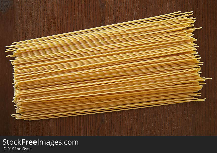 A pile of dried spaghetti noodles on a wood background. A pile of dried spaghetti noodles on a wood background