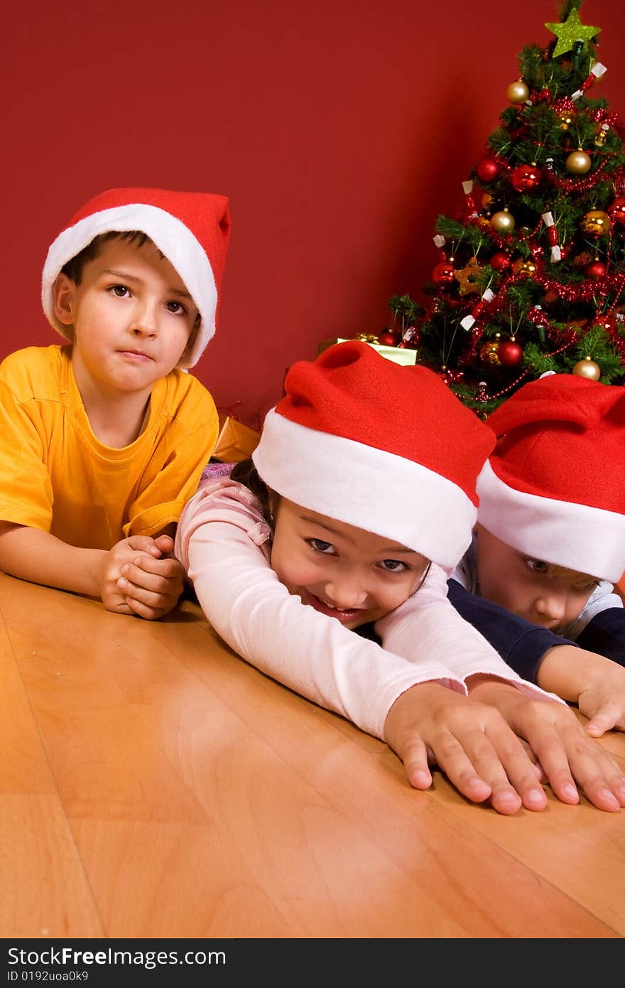 Little children as Santa in red cap laying on the floor with Christmas tree