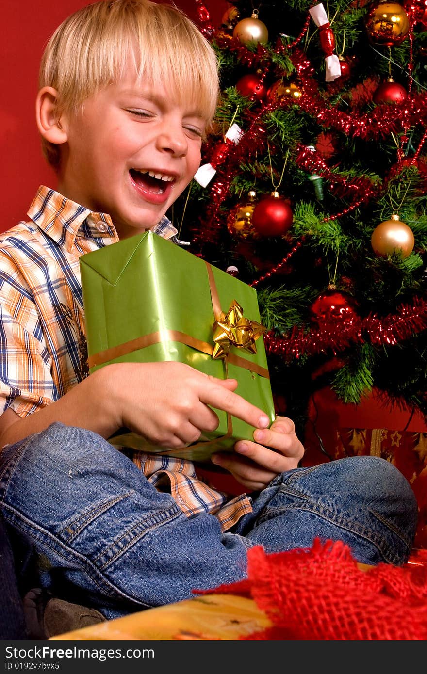 Laughing boy carrying green gift in front of a Christmas Tree. Laughing boy carrying green gift in front of a Christmas Tree.