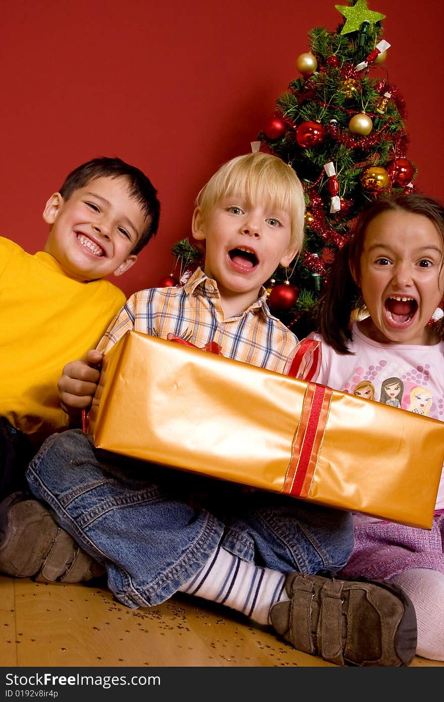 Laughing children carrying gift in front of a Christmas Tree. Laughing children carrying gift in front of a Christmas Tree.