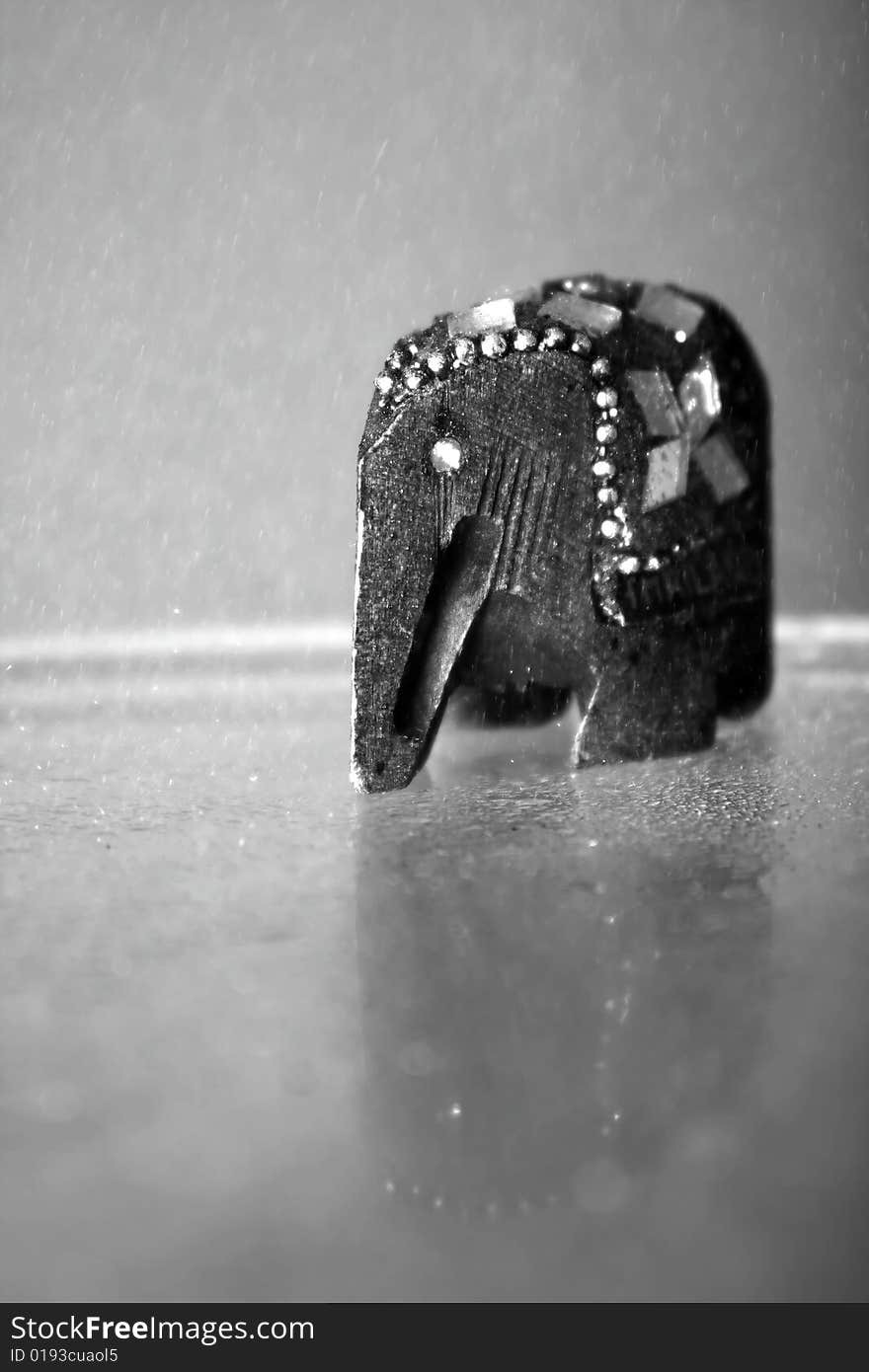 A photograph of a wooden elephant placed on glass table while sprinkled. A photograph of a wooden elephant placed on glass table while sprinkled.