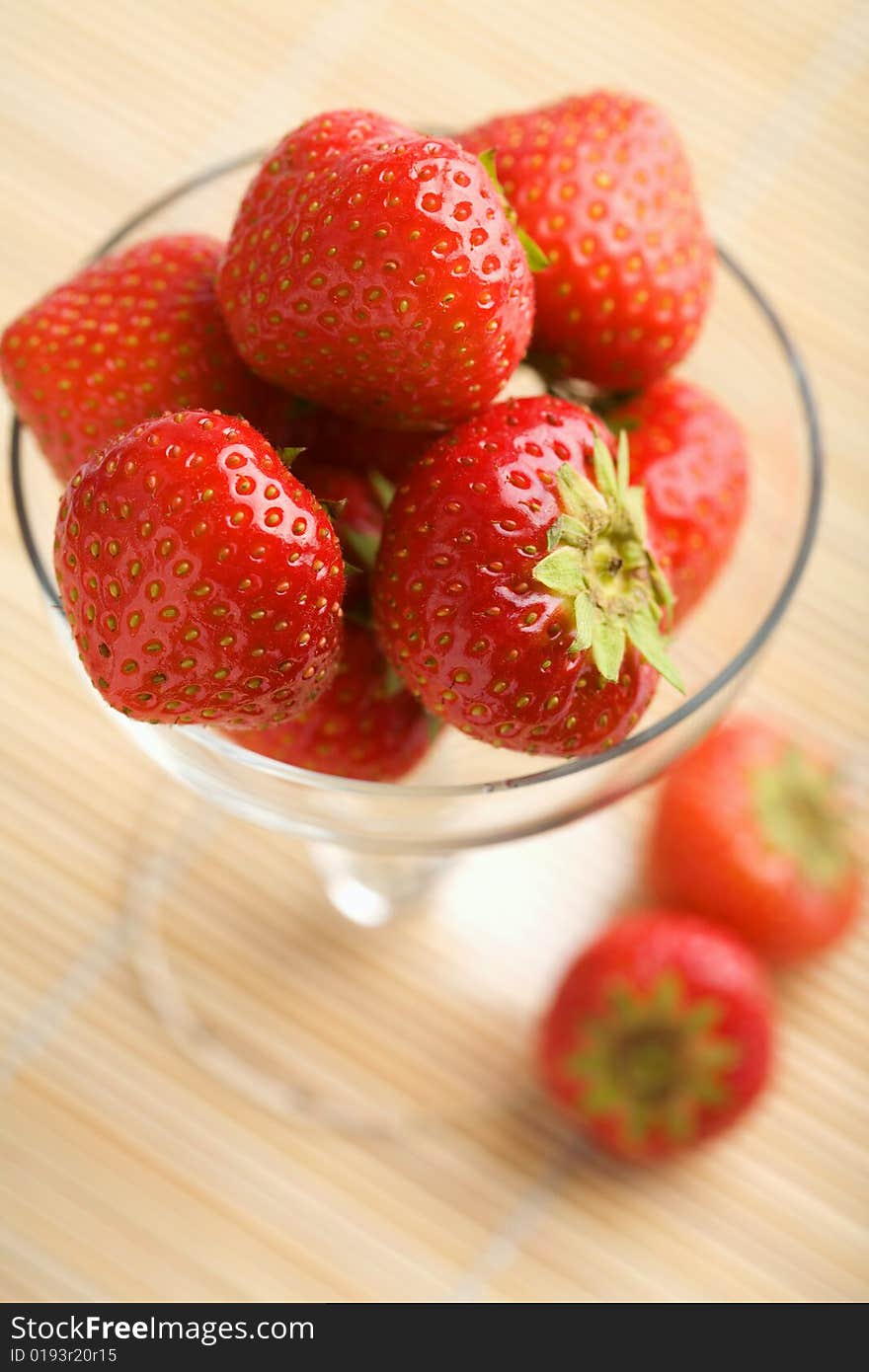 Ripe strawberries in glass bowl over bamboo mat