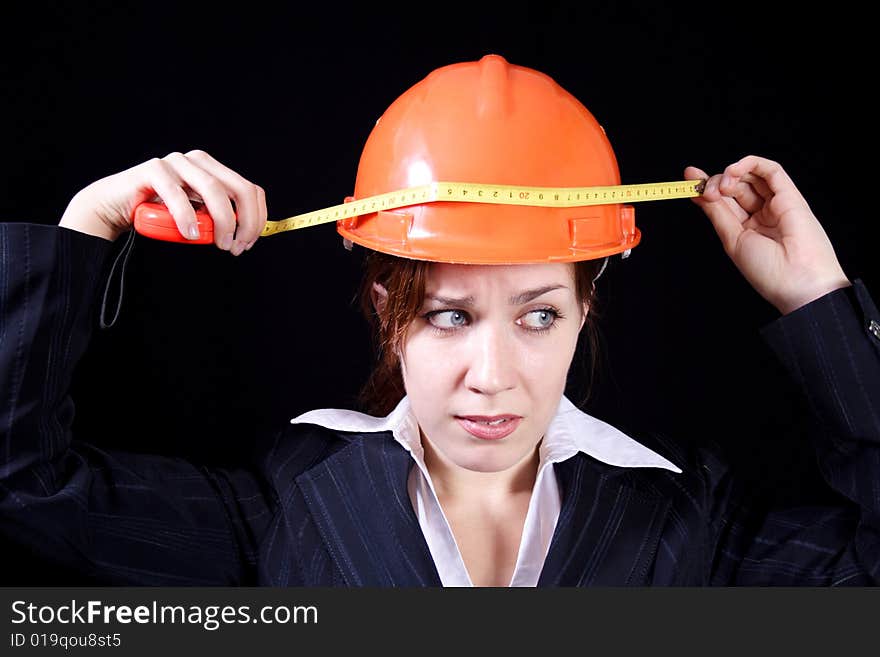 Girl measures by a roulette the helmet on a black background. Girl measures by a roulette the helmet on a black background