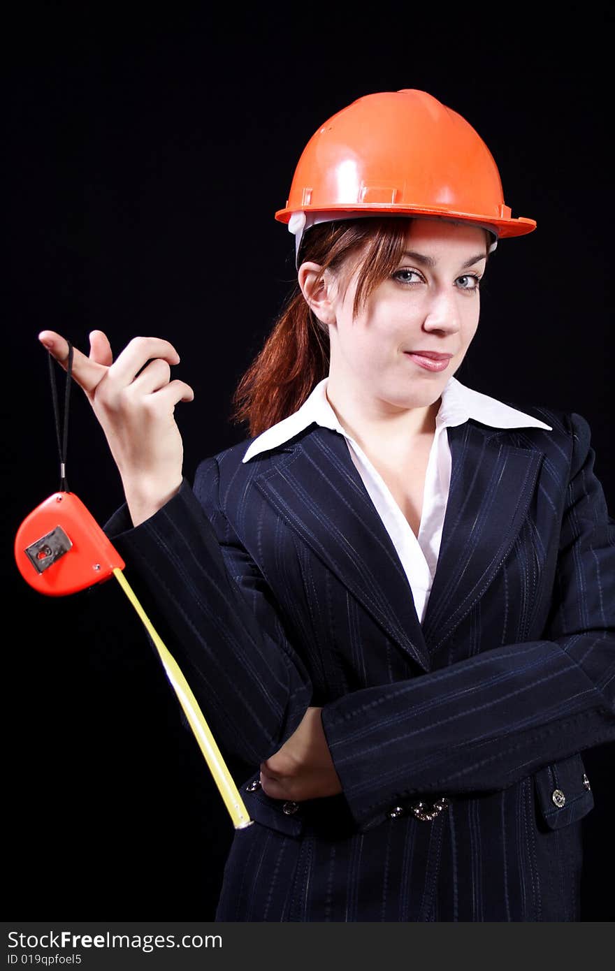 Girl in a business suit with a roulette and in a helmet on a black background. Girl in a business suit with a roulette and in a helmet on a black background