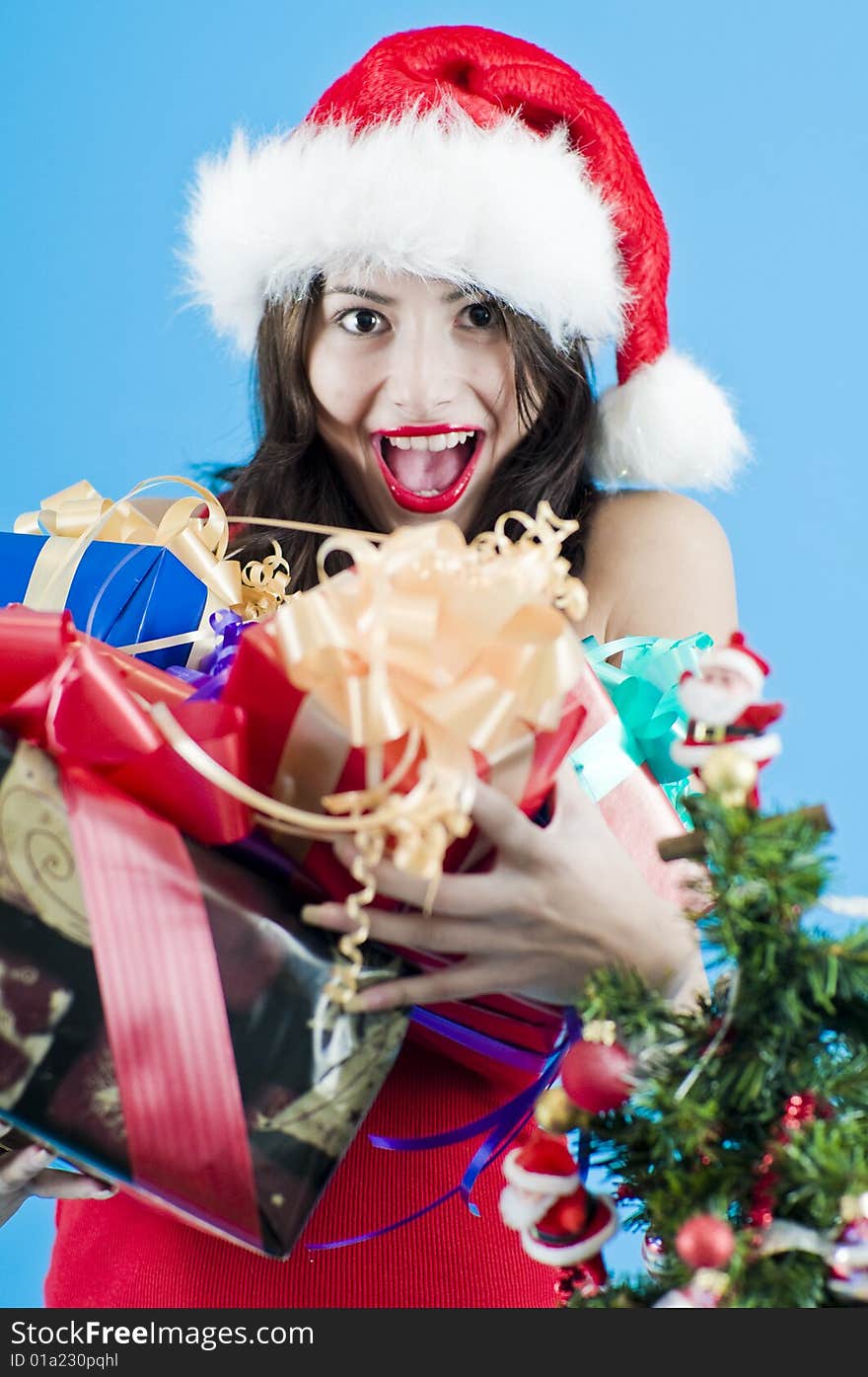 Half body portrait of smiling pretty teenage girl holding Christmas presents and wearing Santa hat, blue background. Half body portrait of smiling pretty teenage girl holding Christmas presents and wearing Santa hat, blue background.