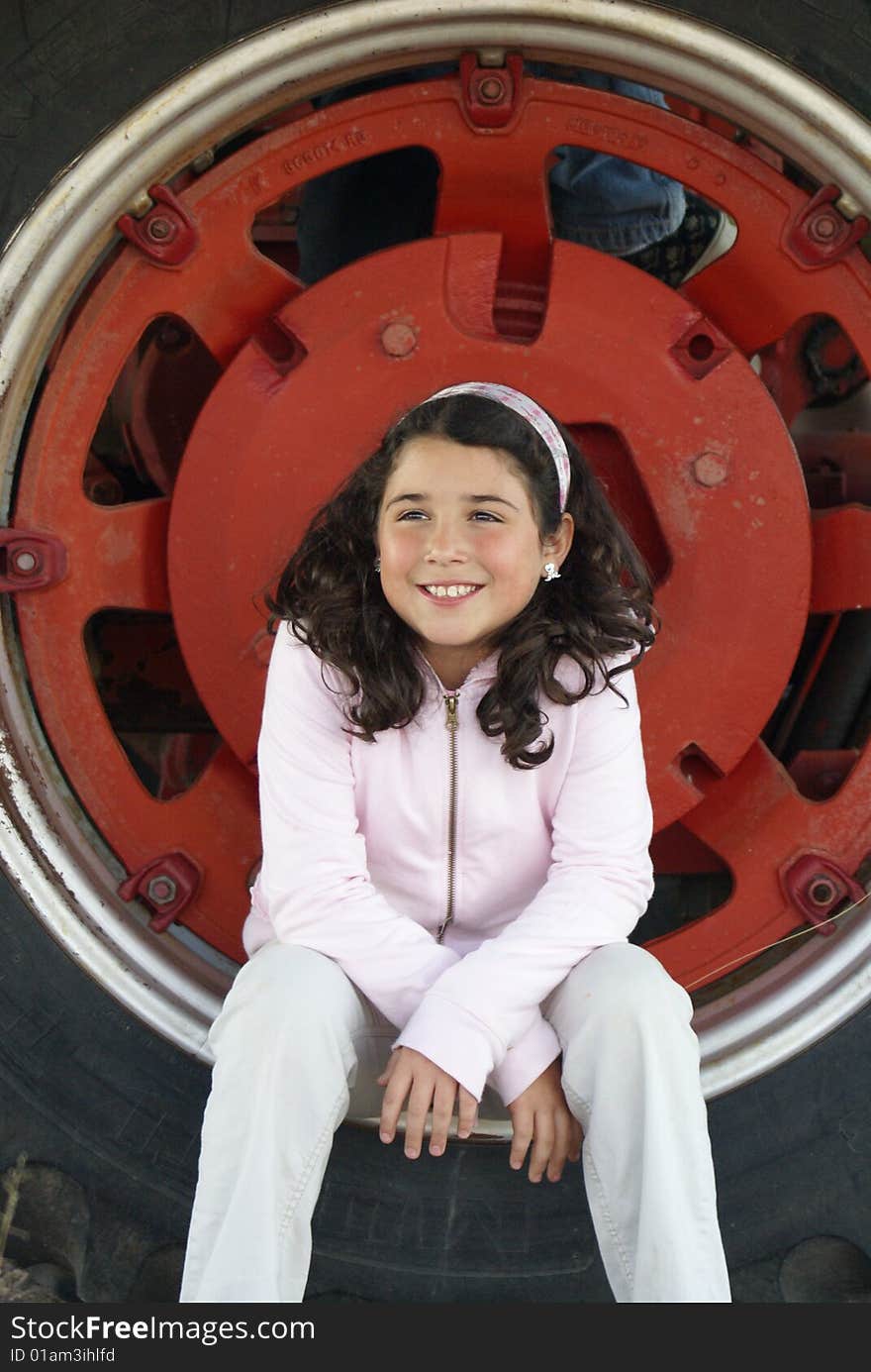 Little girl setting in the wheel of a big red tractor. Little girl setting in the wheel of a big red tractor