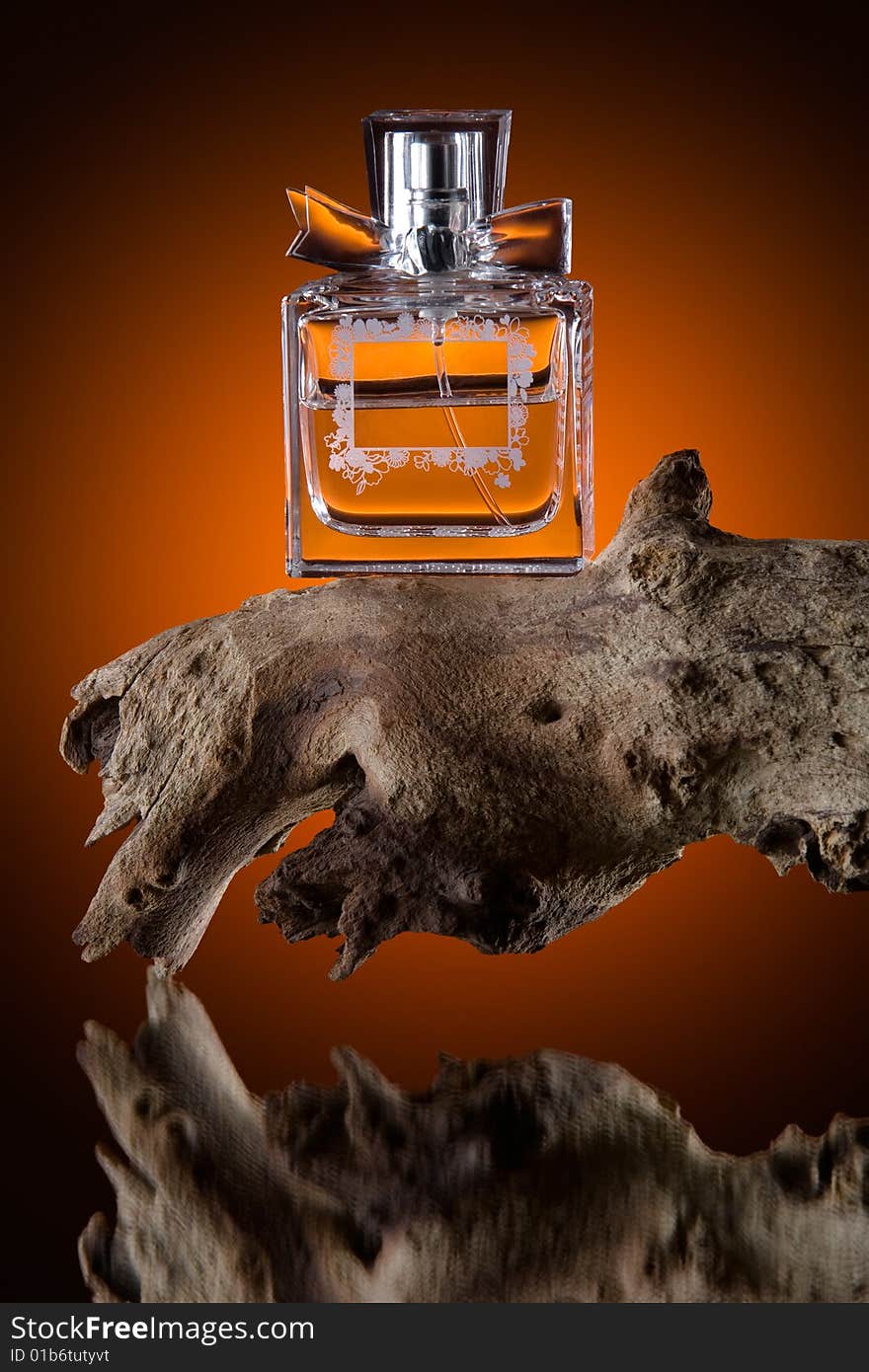 Still life view of luxurious perfume bottle on lump of wood, reflecting on orange tinted background.