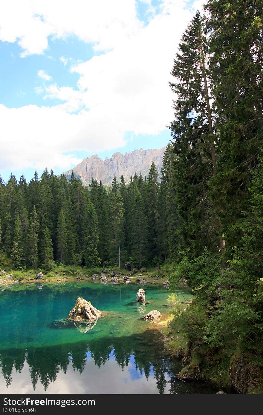 Green pines woods, blue turqoise Carezza  lake & view on Sella montain group, Italy. Green pines woods, blue turqoise Carezza  lake & view on Sella montain group, Italy