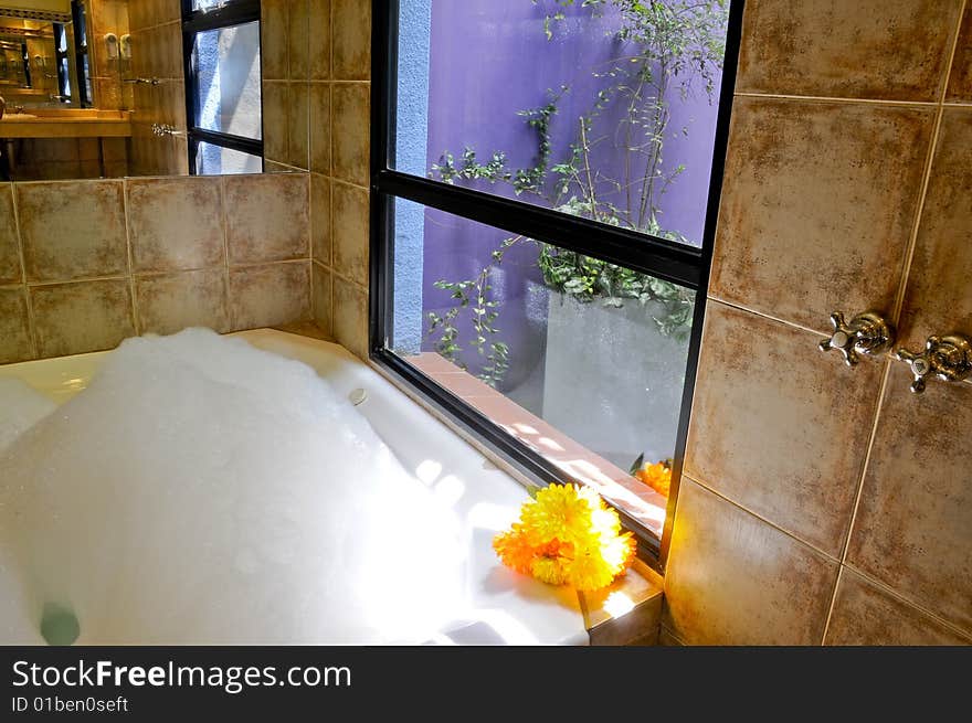 Interior of modern bathroom with jacuzzi full of bubbles. Small flower set.