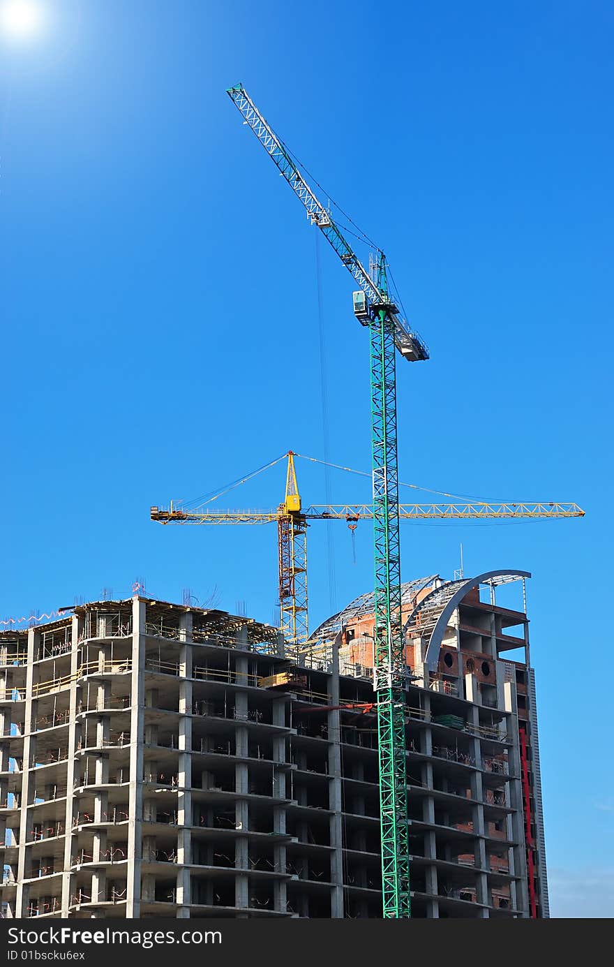 Unfinished building with cranes on blue sky background