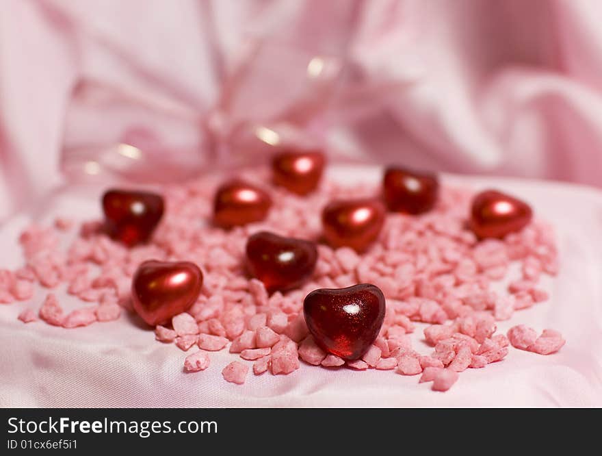 Valentine still life - red glittering hearts lying on pink stones, pink satin and subtle ribbon in the background. Valentine still life - red glittering hearts lying on pink stones, pink satin and subtle ribbon in the background.