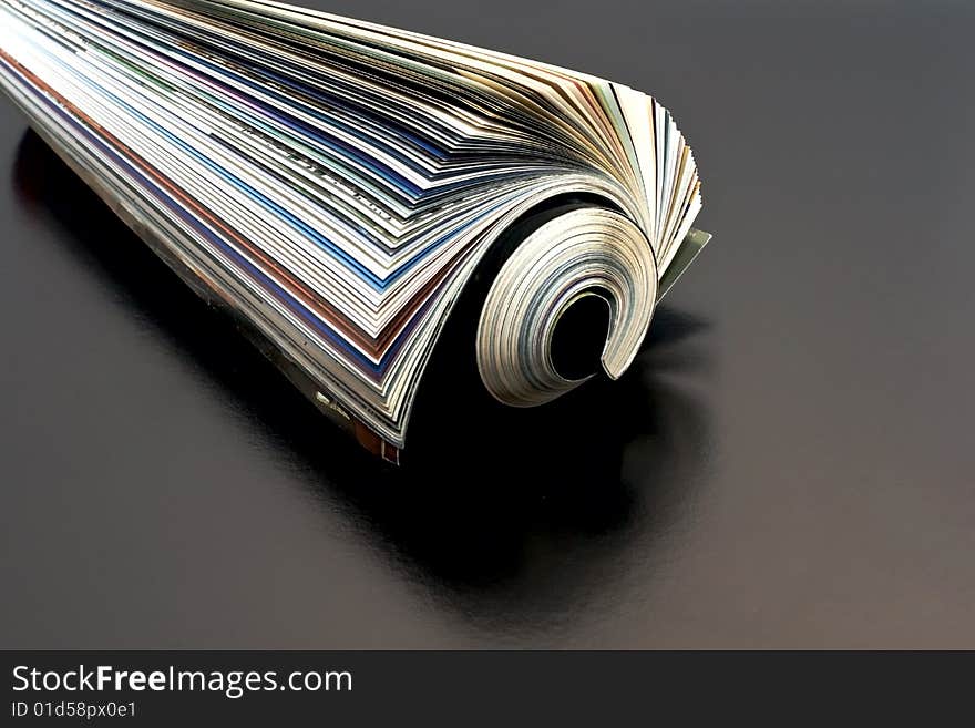 Newspaper rolled up dark background isolate.