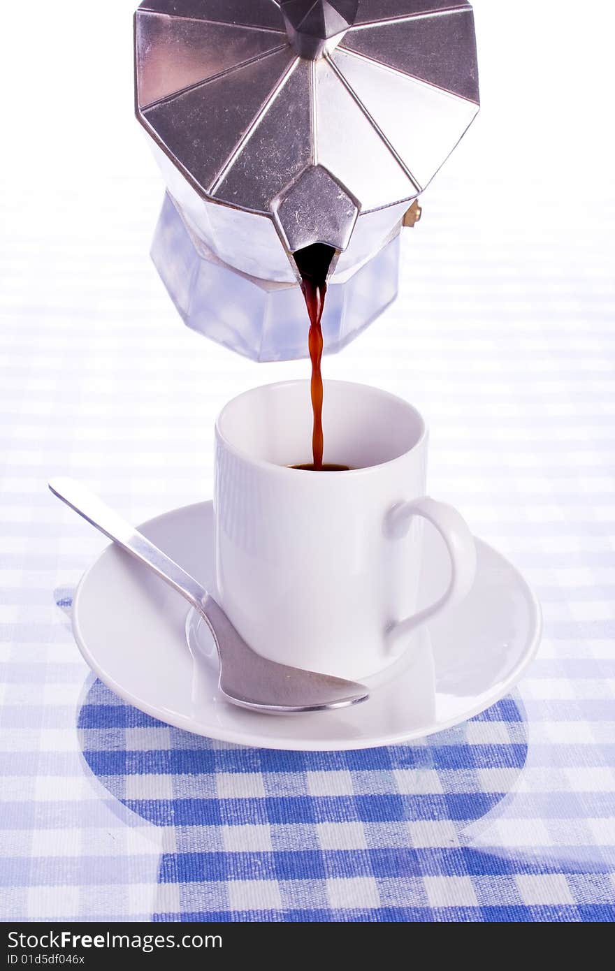 Silver espresso maker pouring coffee into white cup reflected on blue checked surface. Silver espresso maker pouring coffee into white cup reflected on blue checked surface