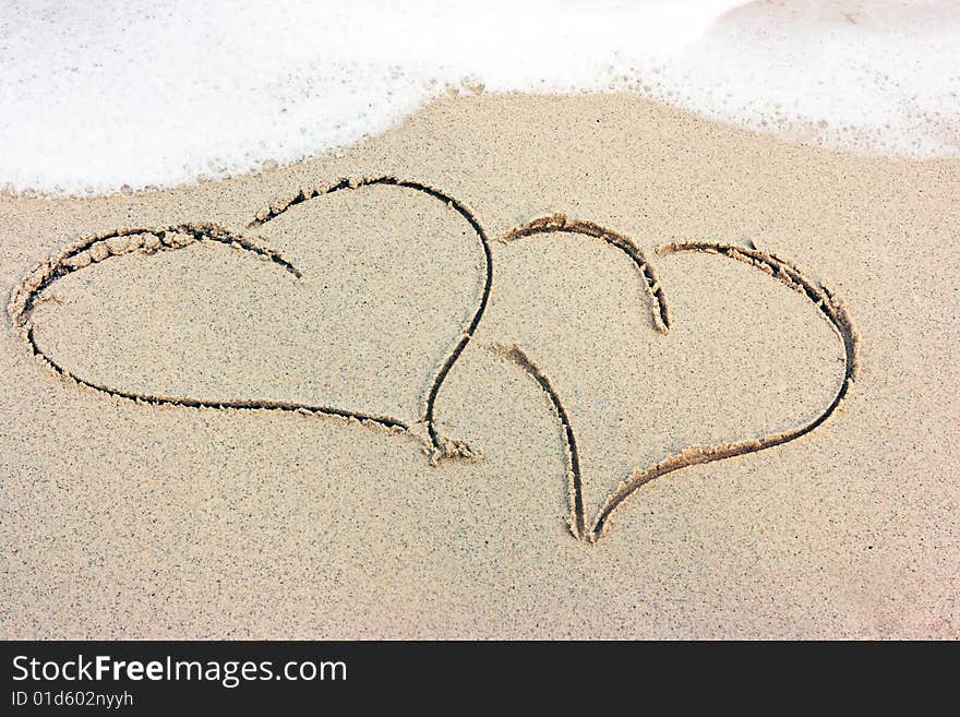 Two hearts drawing on the sandy beach