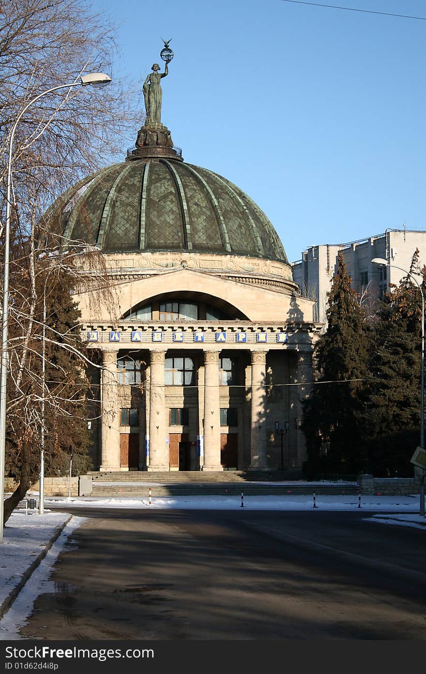 Building of a planetarium with a dome and a statue above on a background of the dark blue sky