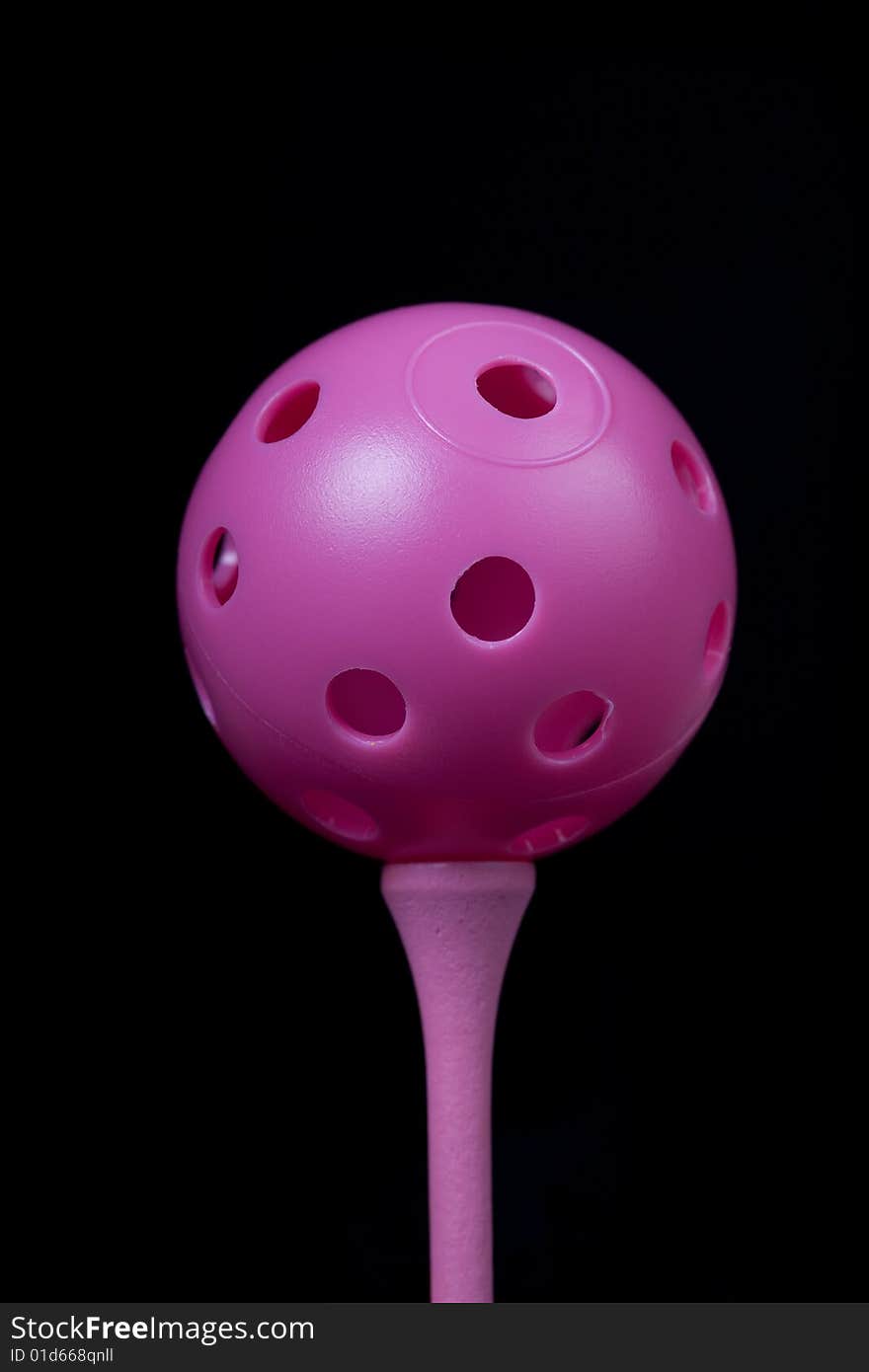 Pink practice ball on golf tee with black background. Pink practice ball on golf tee with black background