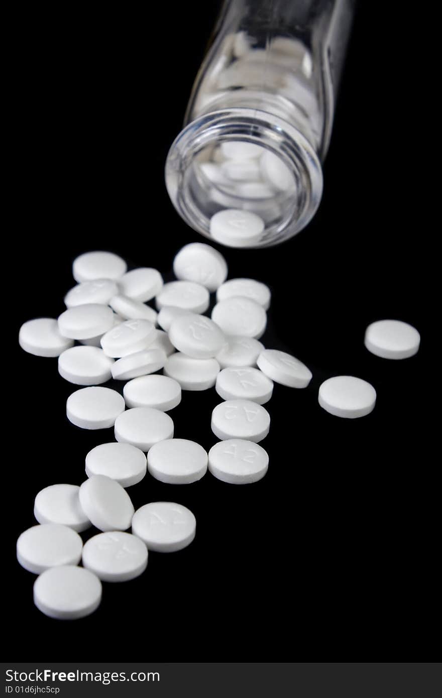 Details of small white pills spilling out of medicine container, isolated on black background. Details of small white pills spilling out of medicine container, isolated on black background