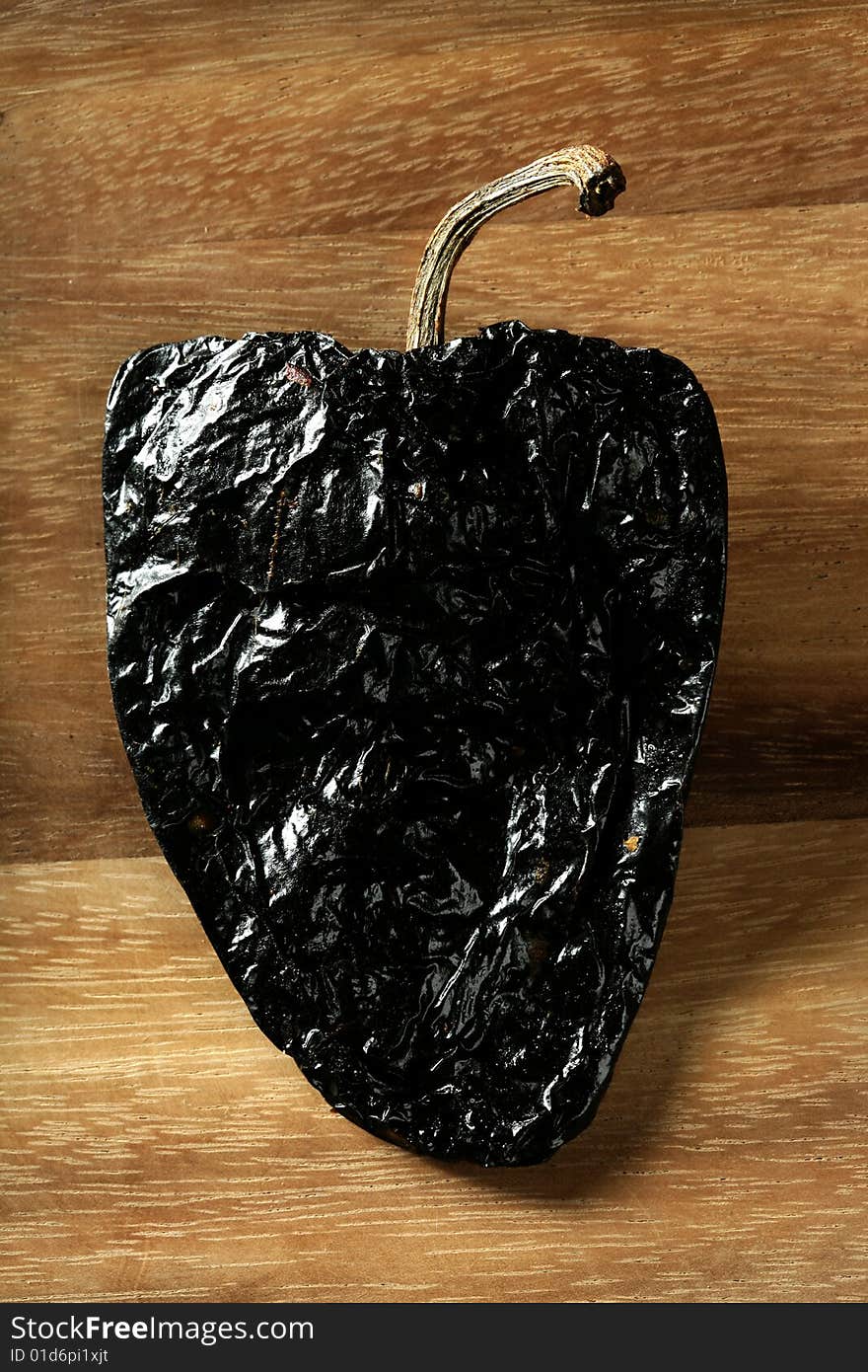 One black mexican dried chili pepper still on warm wood background