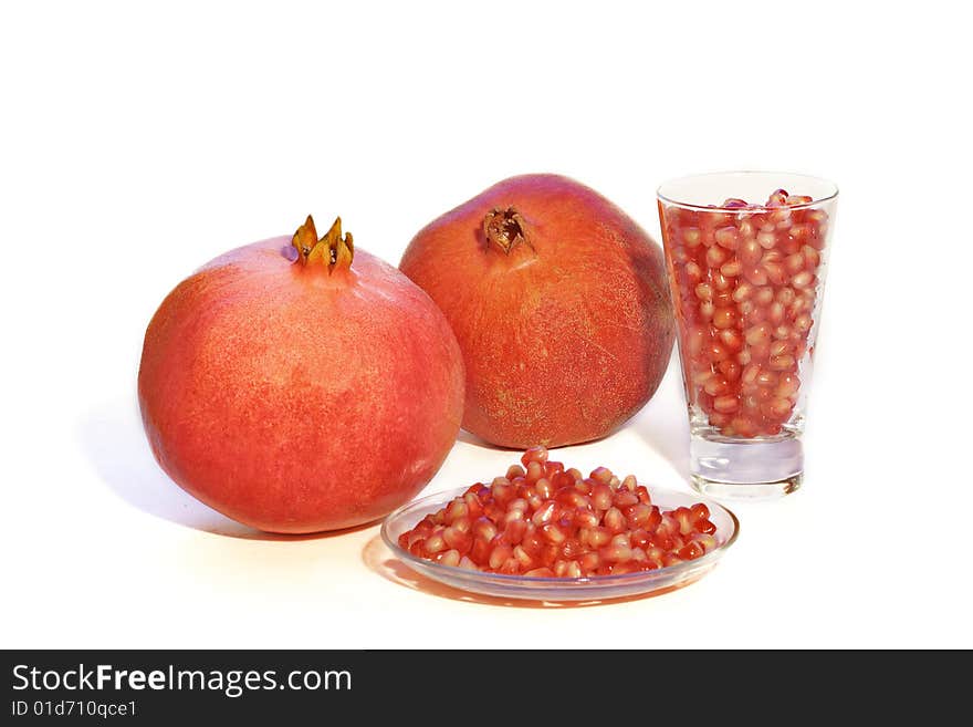 Pomegranates on white background with seeds in  glass and on the plate. Pomegranates on white background with seeds in  glass and on the plate