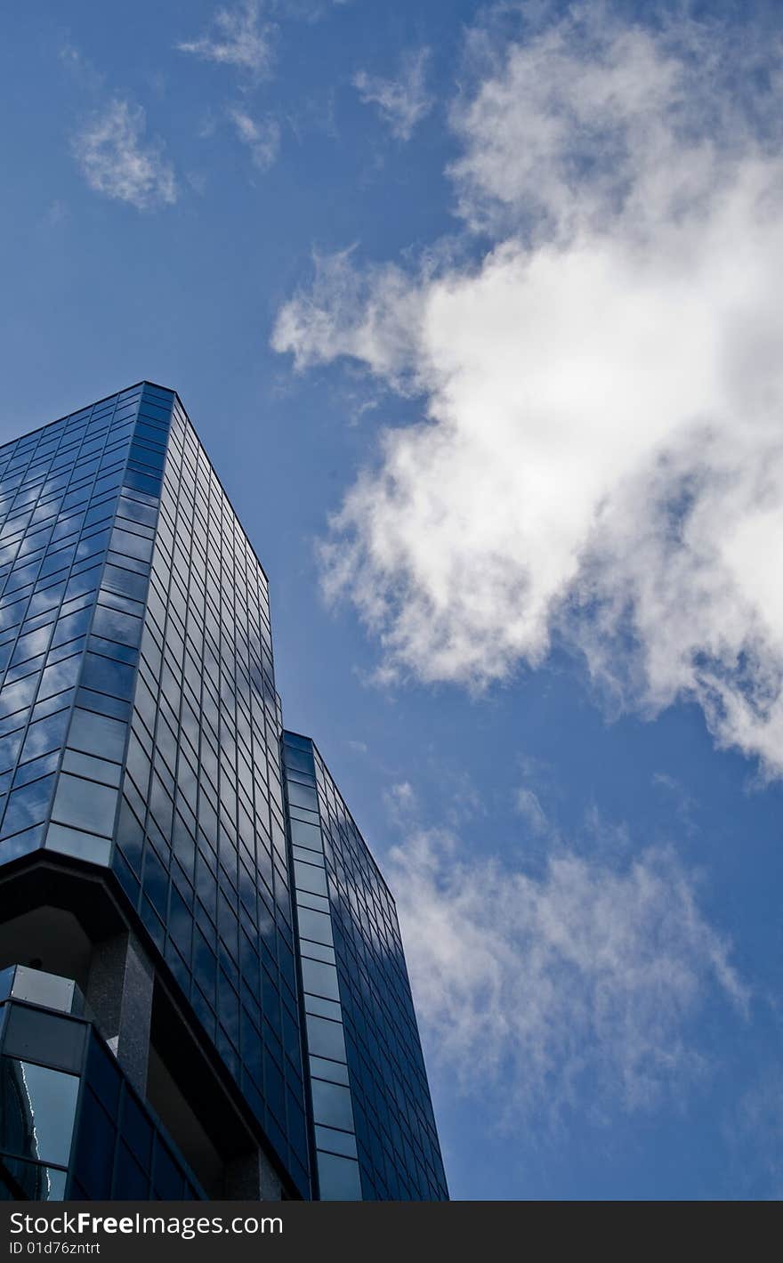 An overhead shot of a single skyscraper with clouds having a bluish tint