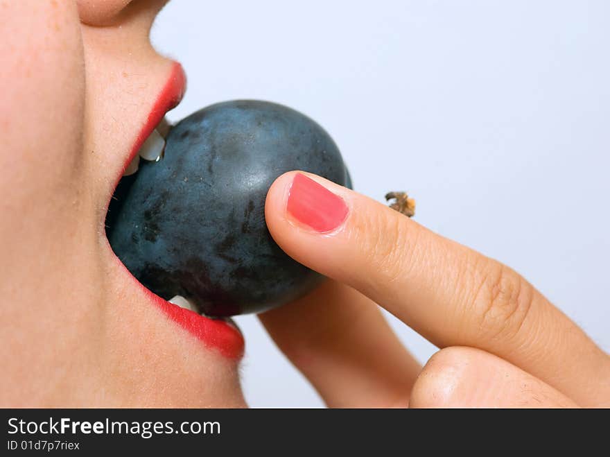 Girl, holding a plum between her teeth, taking a bite. Girl, holding a plum between her teeth, taking a bite