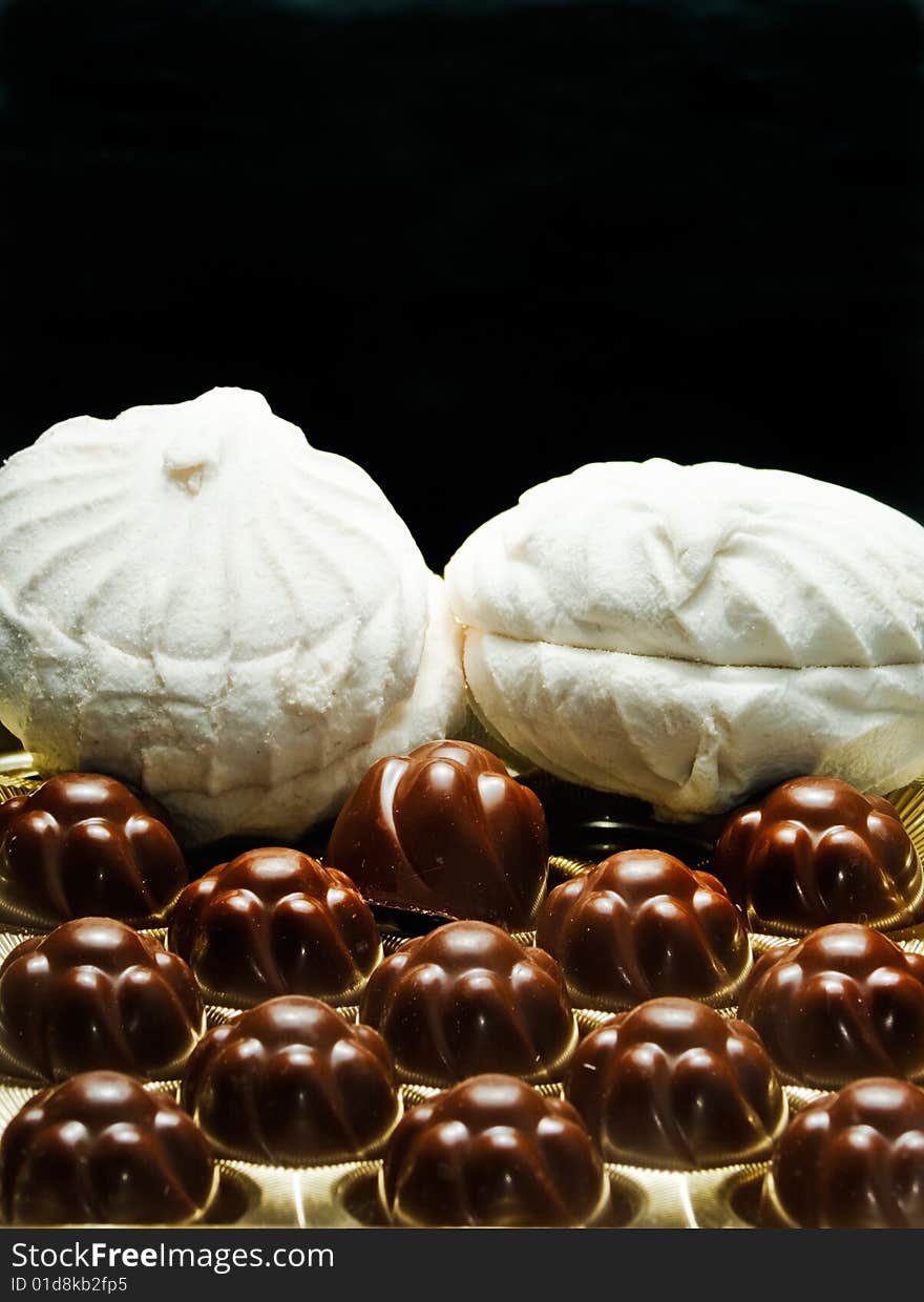 Chocolates and soft white marshmallows on a black background