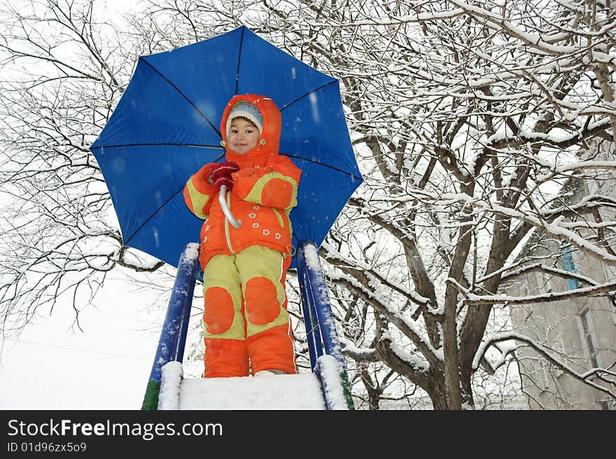 Child in red overalls on background of the blue umbrella