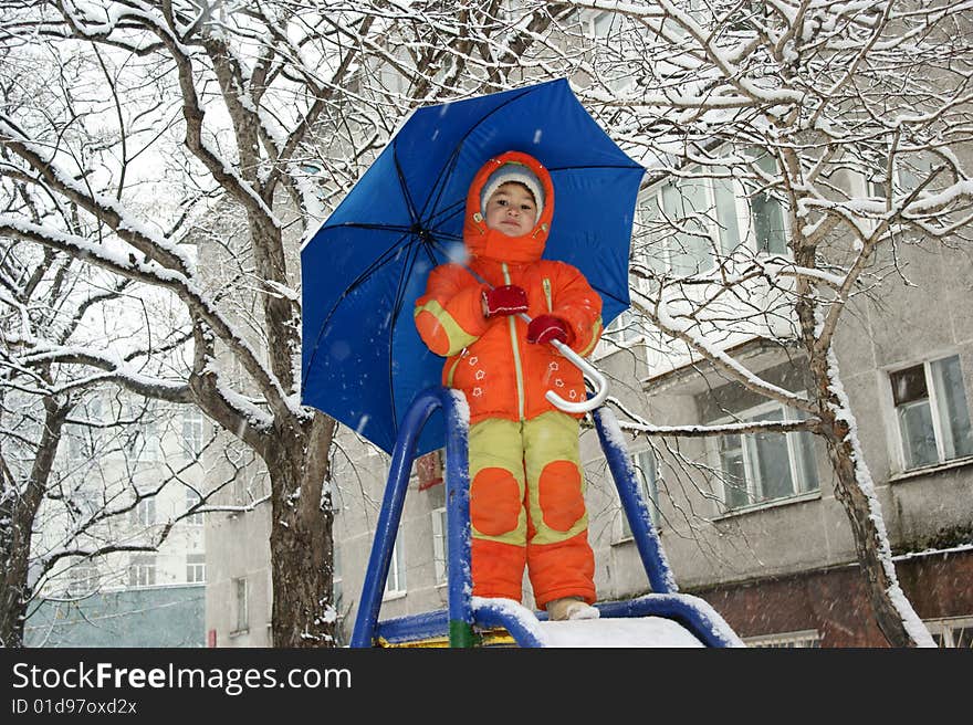 Child in red overalls on background of the blue umbrella