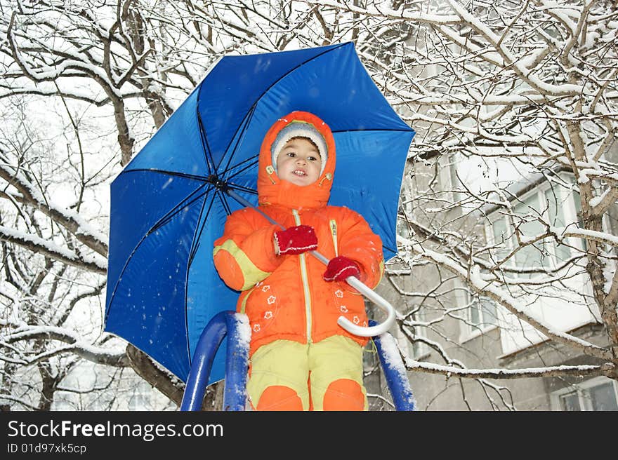 Child in red overalls on background of the blue umbrella