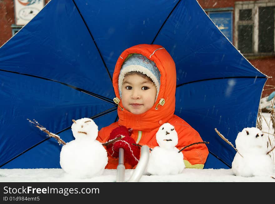 Child in red overalls on background of the blue umbrella