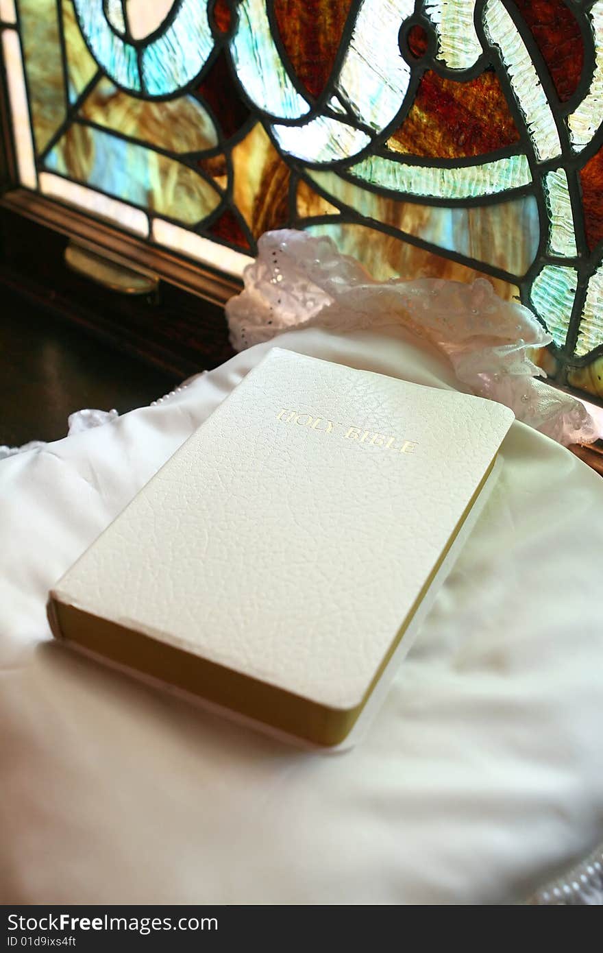 White bible on satin pillow with stained glass in background. White bible on satin pillow with stained glass in background