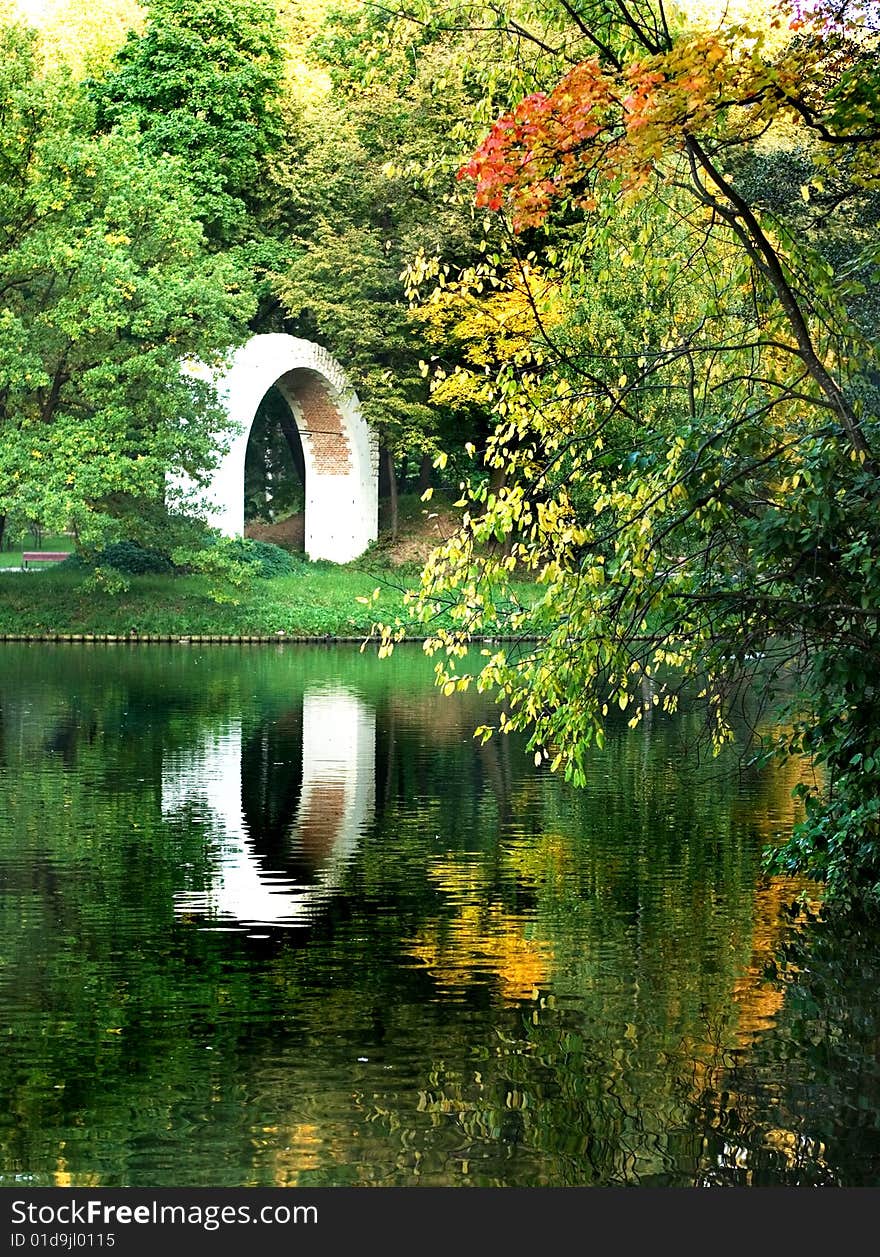 A park lake with yellow trees and stone ruins reflecting in water. A park lake with yellow trees and stone ruins reflecting in water