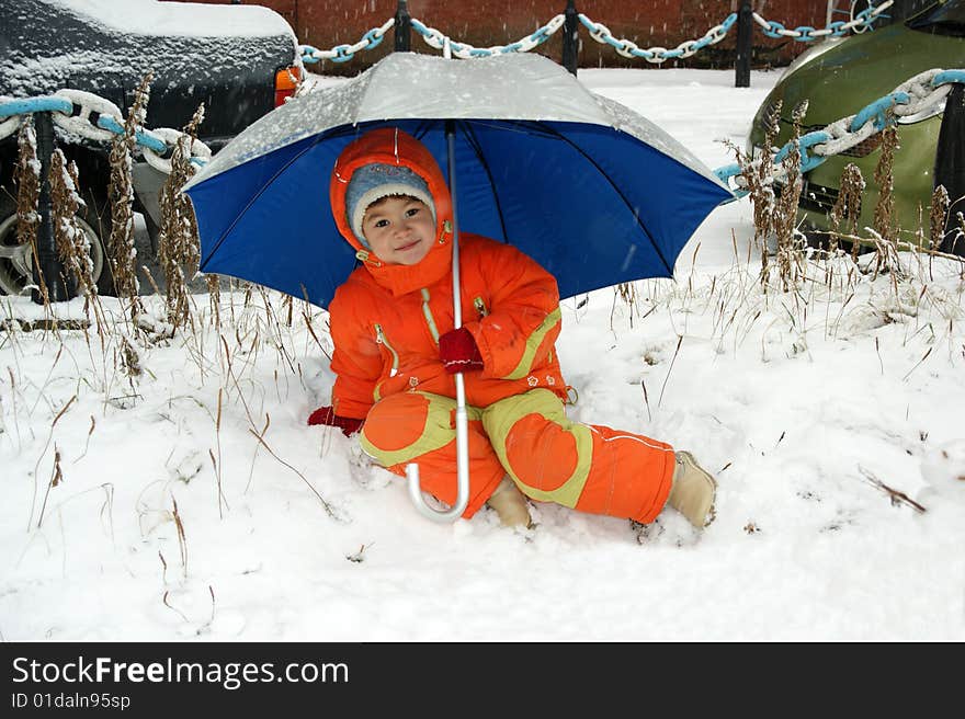 Child in red overalls on background of the blue umbrella